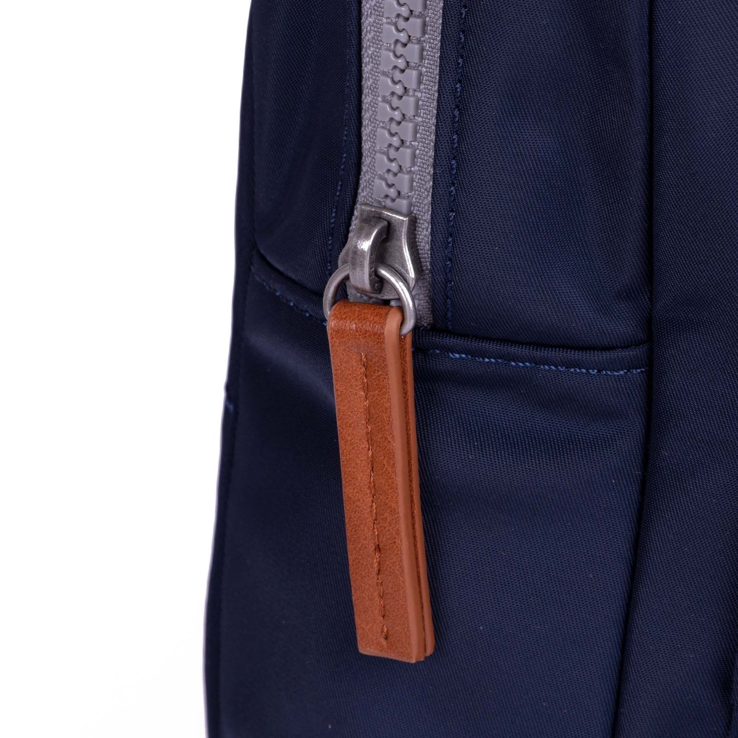 Dark blue sling bag close-up of zipper track and tan leather-style pull tab