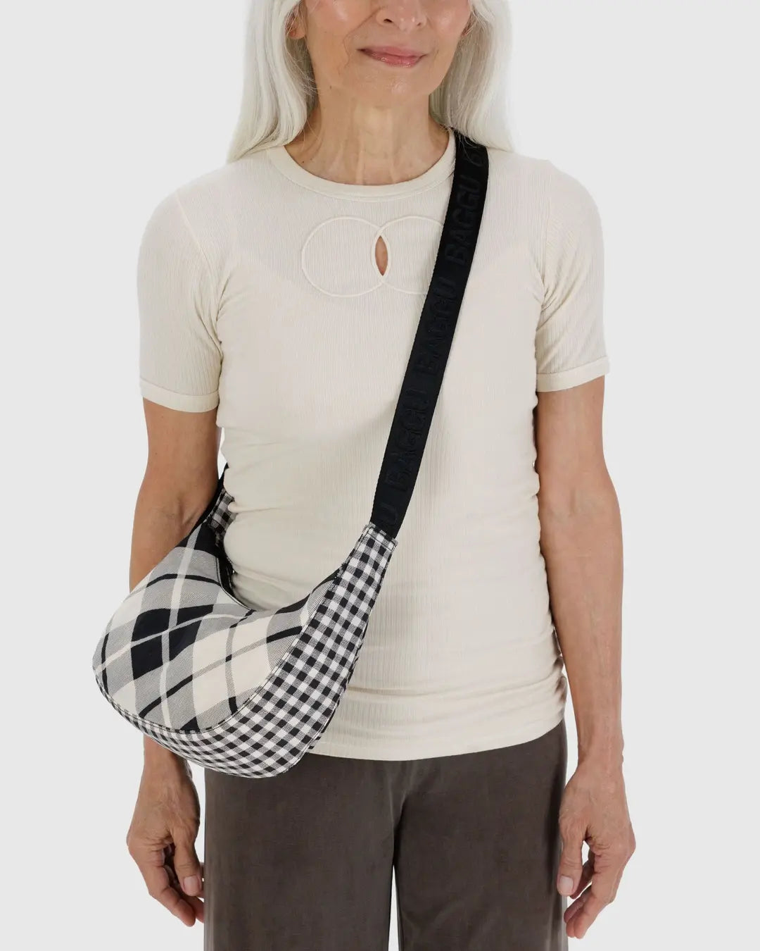 Small crescent nylon crossbody bag in black with plaid panel, worn diagonally