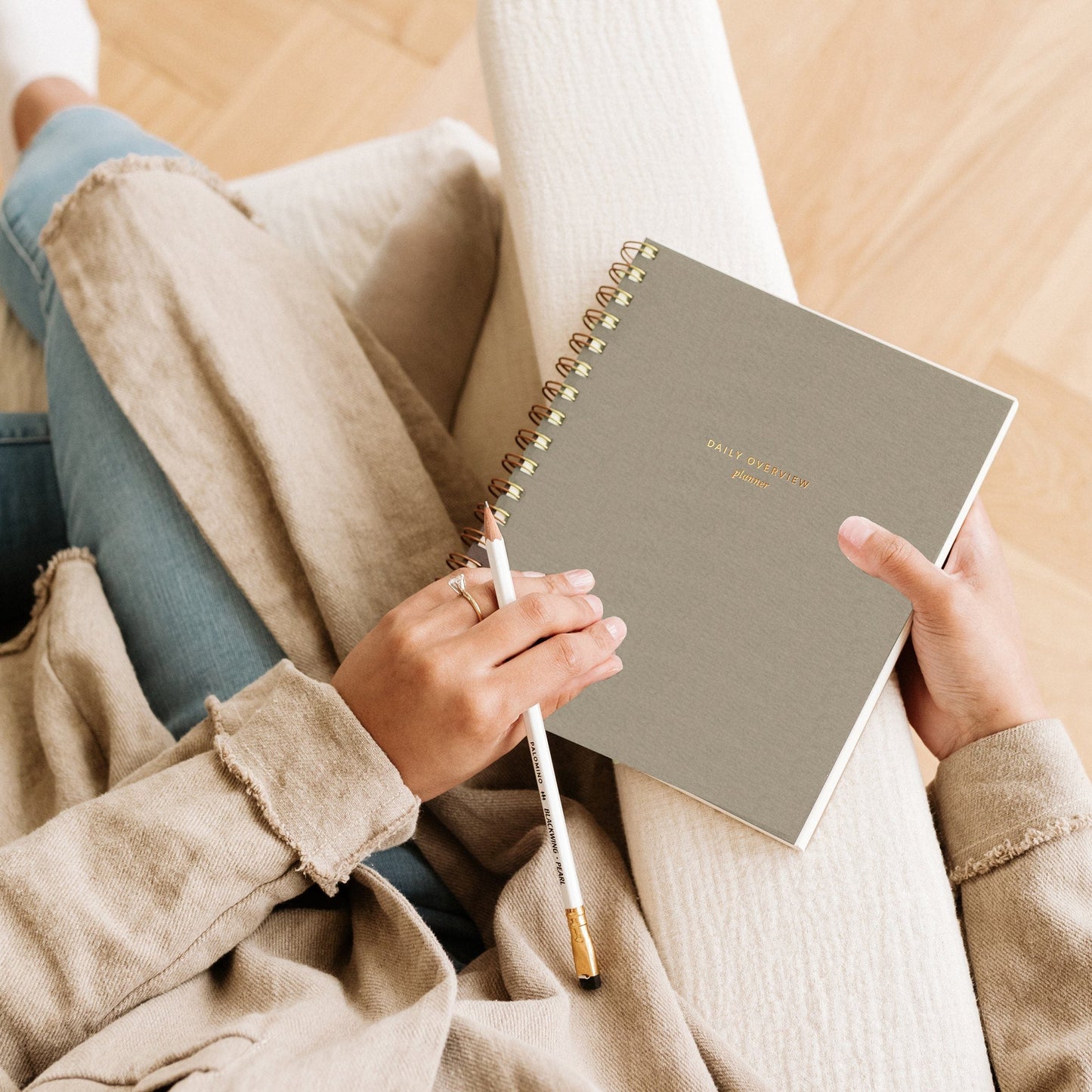 Spiral-bound daily overview planner in taupe, held open with pen