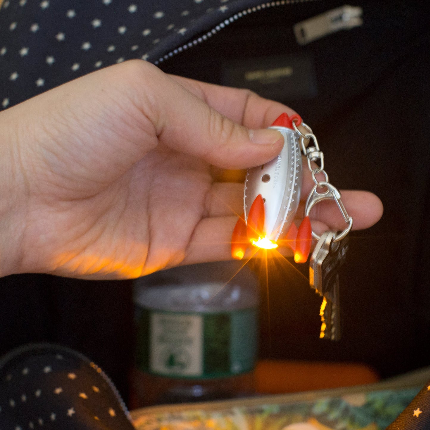 Rocket LED keychain glowing with red fins; silver body, blue window, and metal keyring