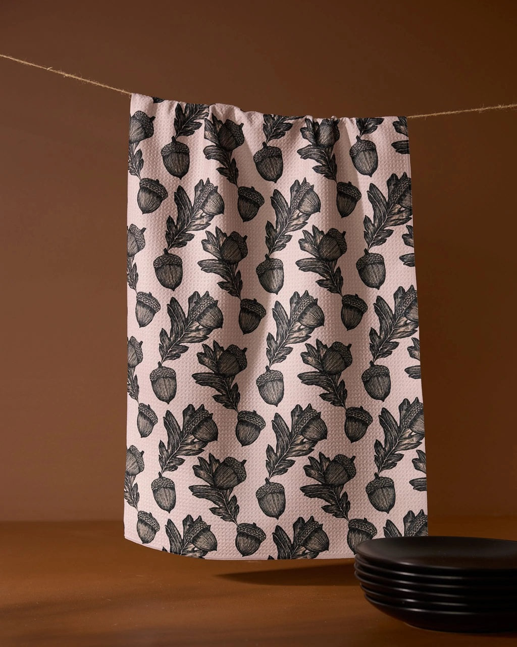 Pink kitchen tea towel with black acorn and leaf botanical pattern, hanging
