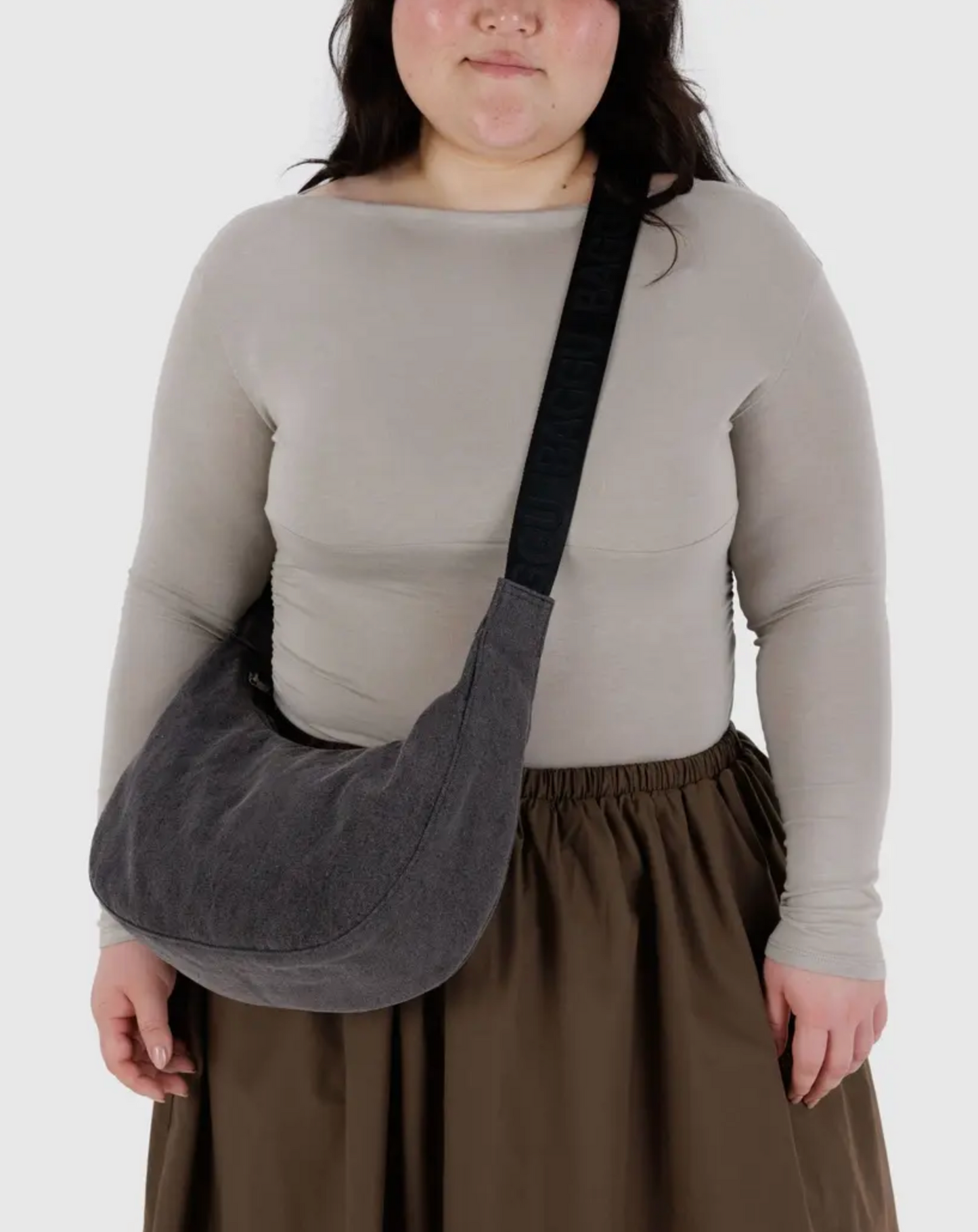 Denim crescent shoulder bag worn crossbody with dark strap and curved silhouette
