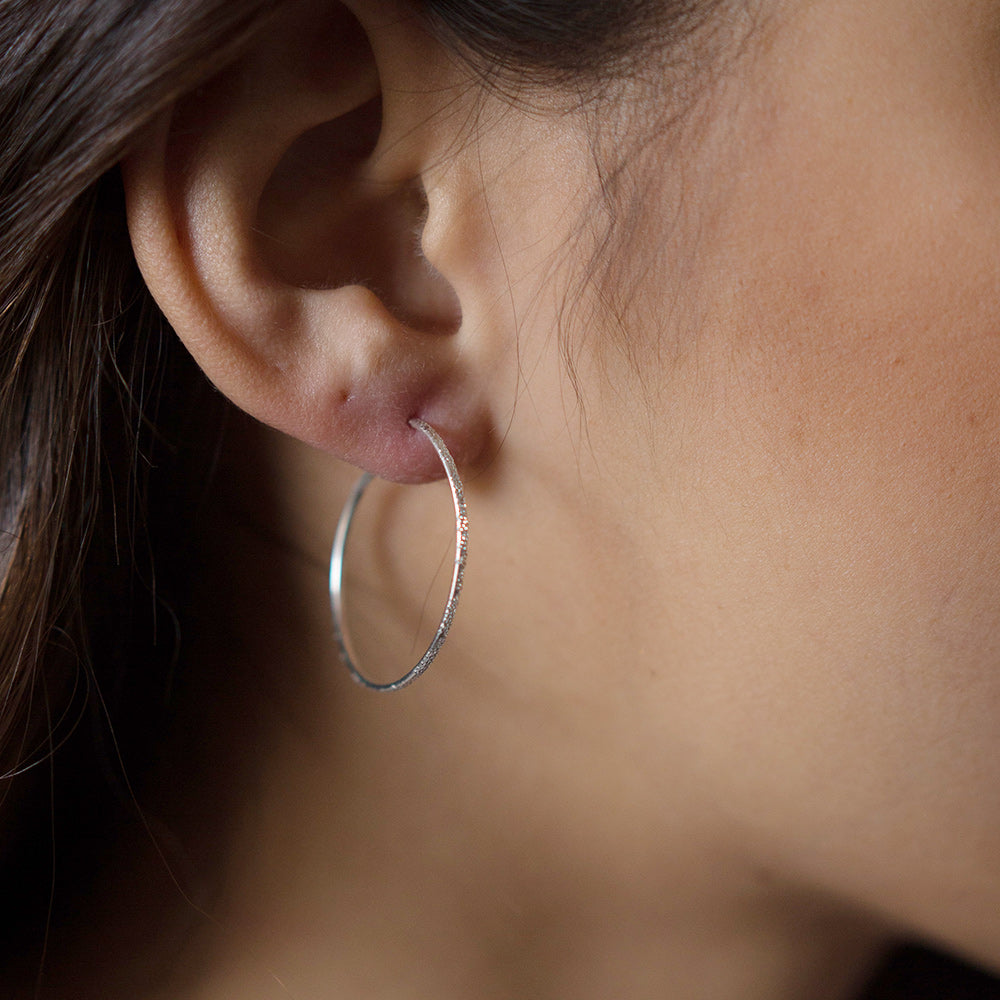 Sterling silver diamond-dusted hoop earring on ear, medium round size
