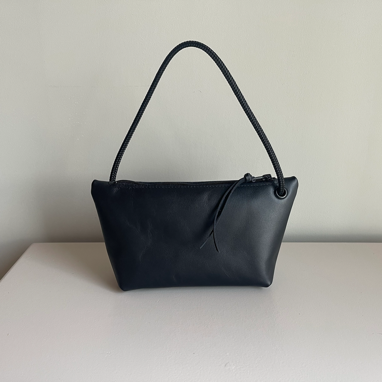 Dark cord pouch with black braided handle and small drawstring tie at top.