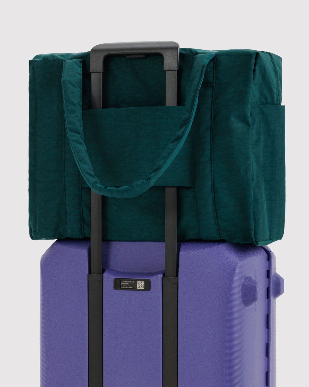Teal carry-on bag fitted over a rolling suitcase handle, showing padded front panel.