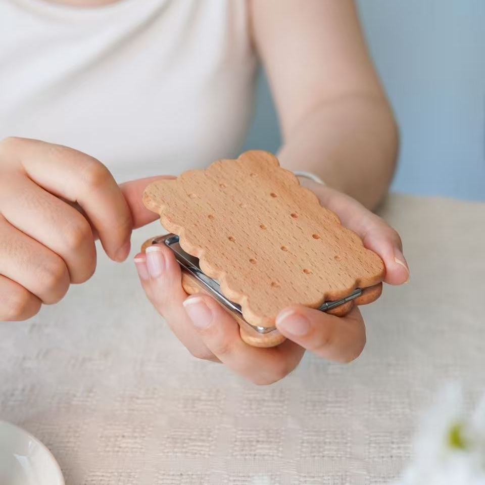 Beech wood biscuit-shaped pocket mirror compact held open, metal hinge visible.