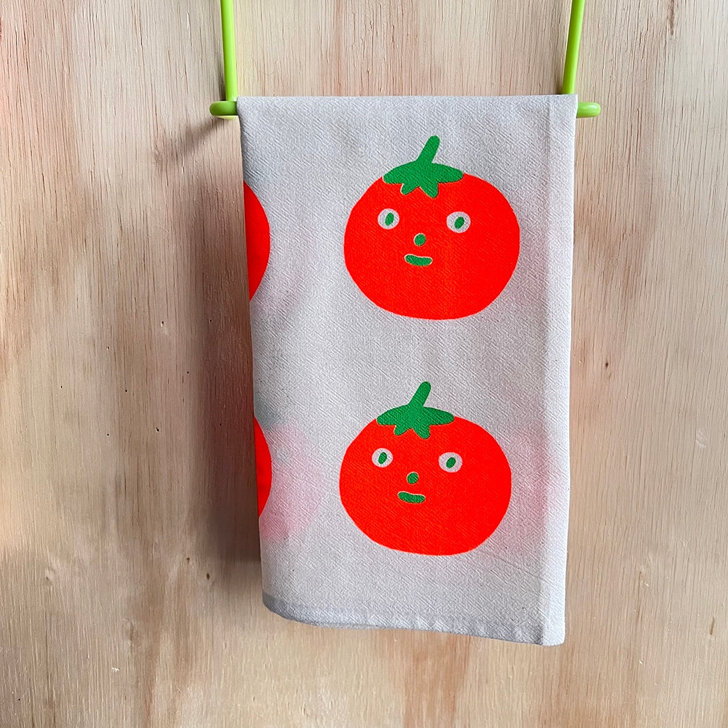 Gray cotton tea towel with two red tomato faces and green leaves, clipped up