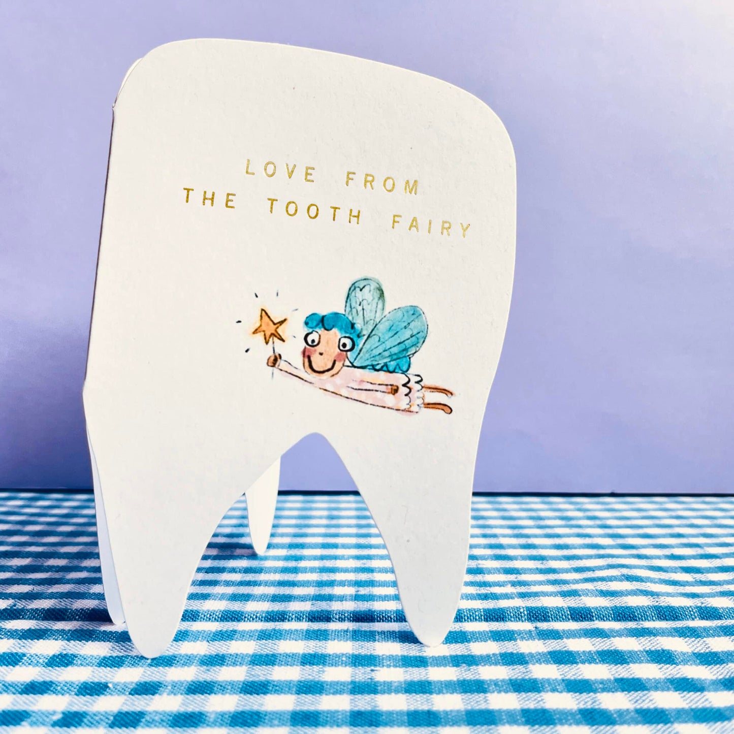 White tooth-shaped tooth fairy card with blue fairy illustration and gold message.