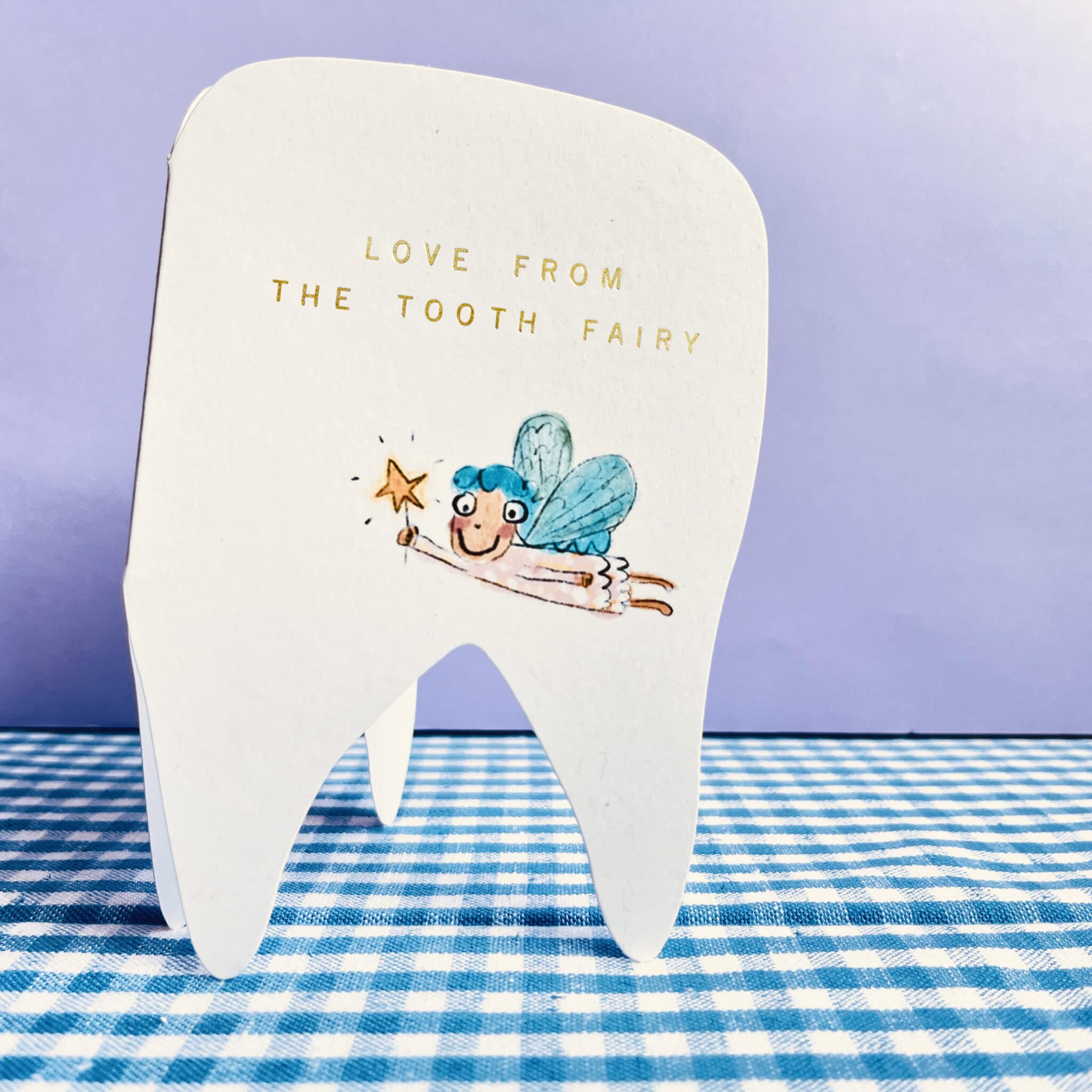 White tooth-shaped tooth fairy card with blue fairy illustration and gold message.