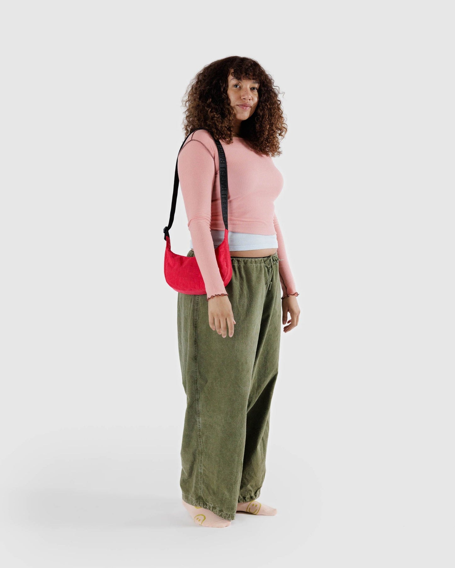 Small crescent nylon crossbody bag in red with top handle and strap tag