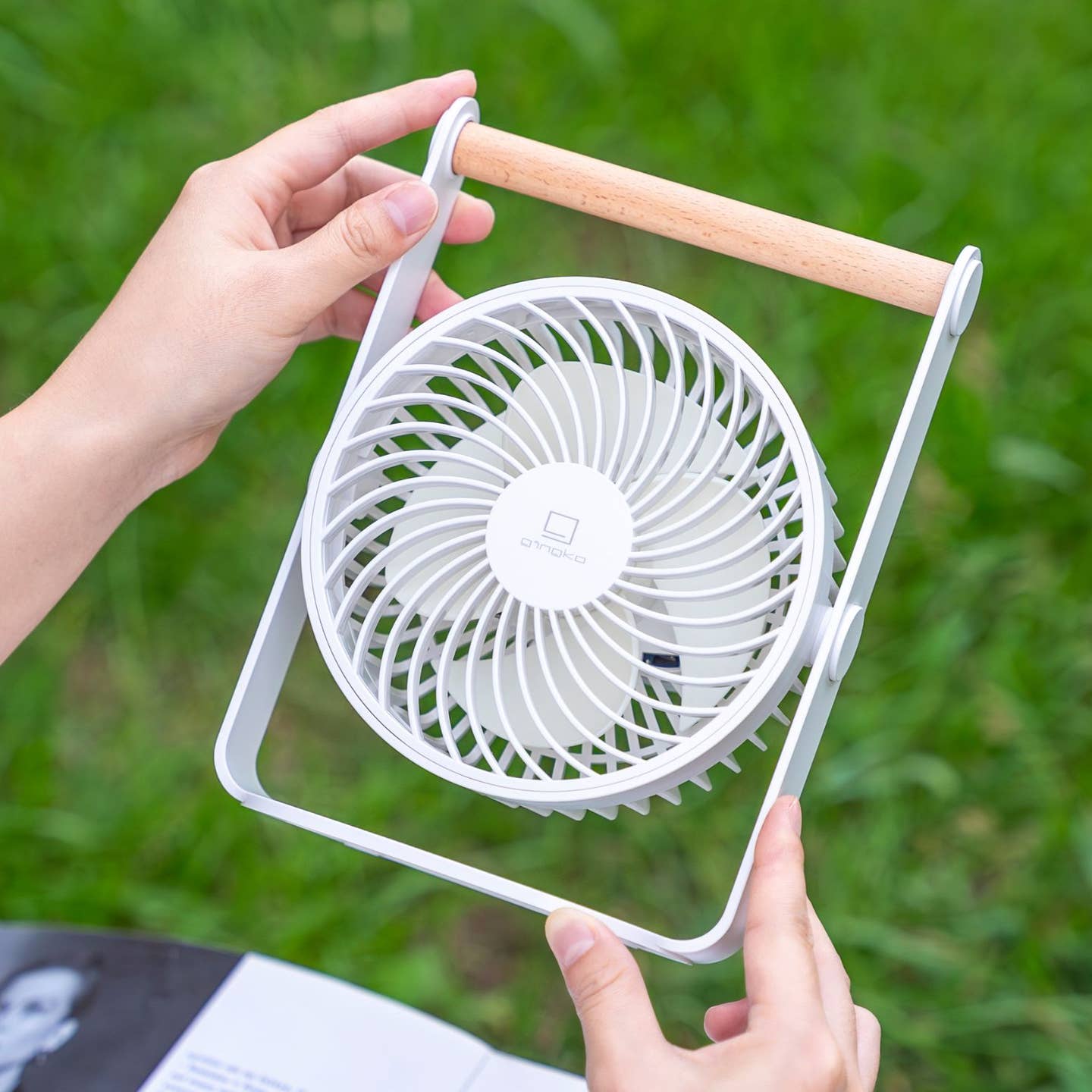 Portable white fan with wooden handle, circular grille held in hands