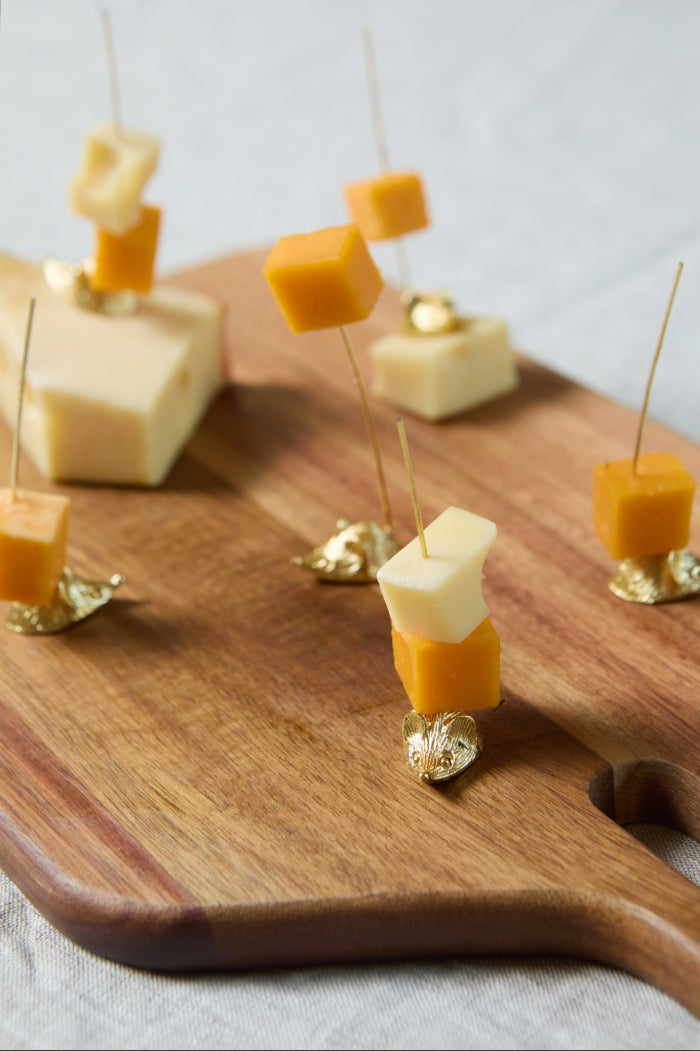 Six hors d'oeuvres picks with gold animal bases inserted into cheese cubes on a board