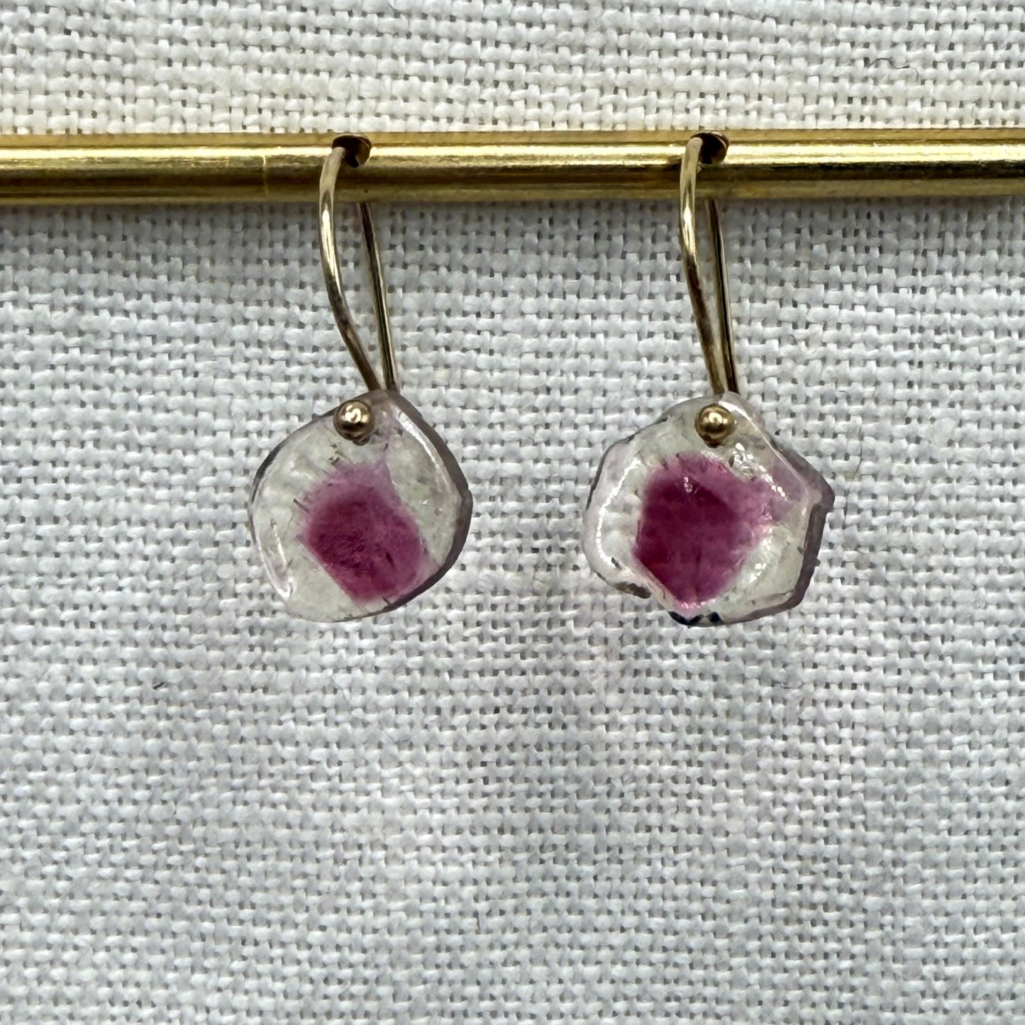 Gold hoop dangle earrings with pink faceted teardrop stones on a bar