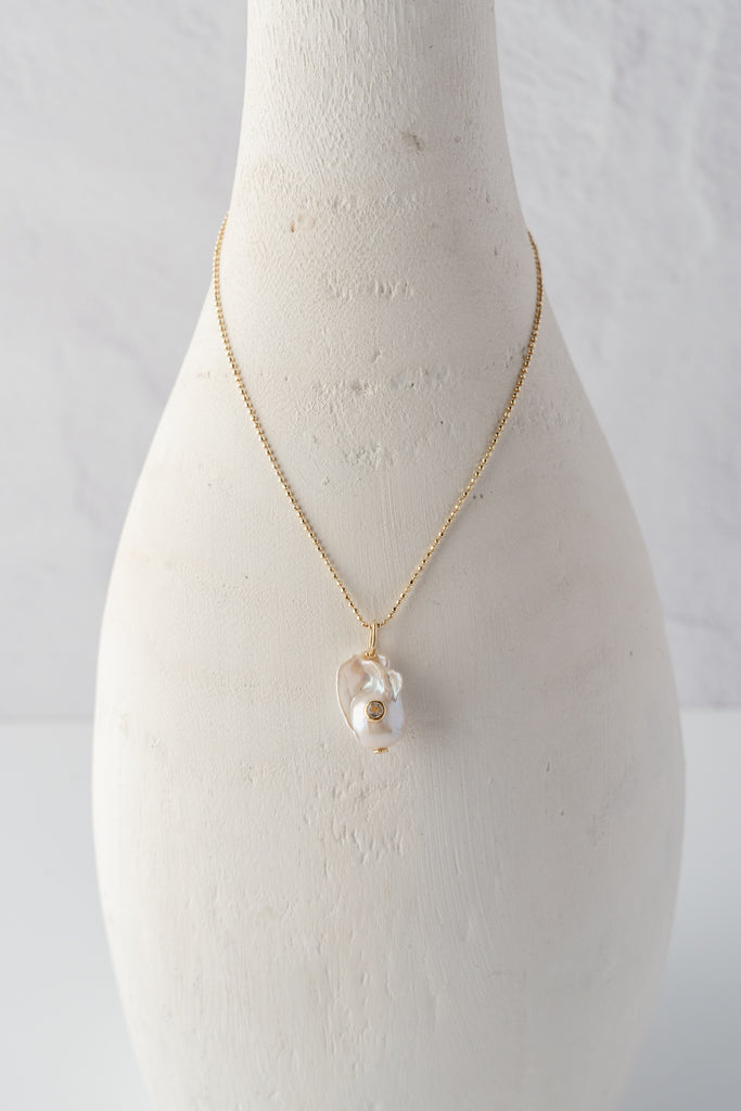 White baroque pearl pendant necklace with gold chain, shown centered on bust.