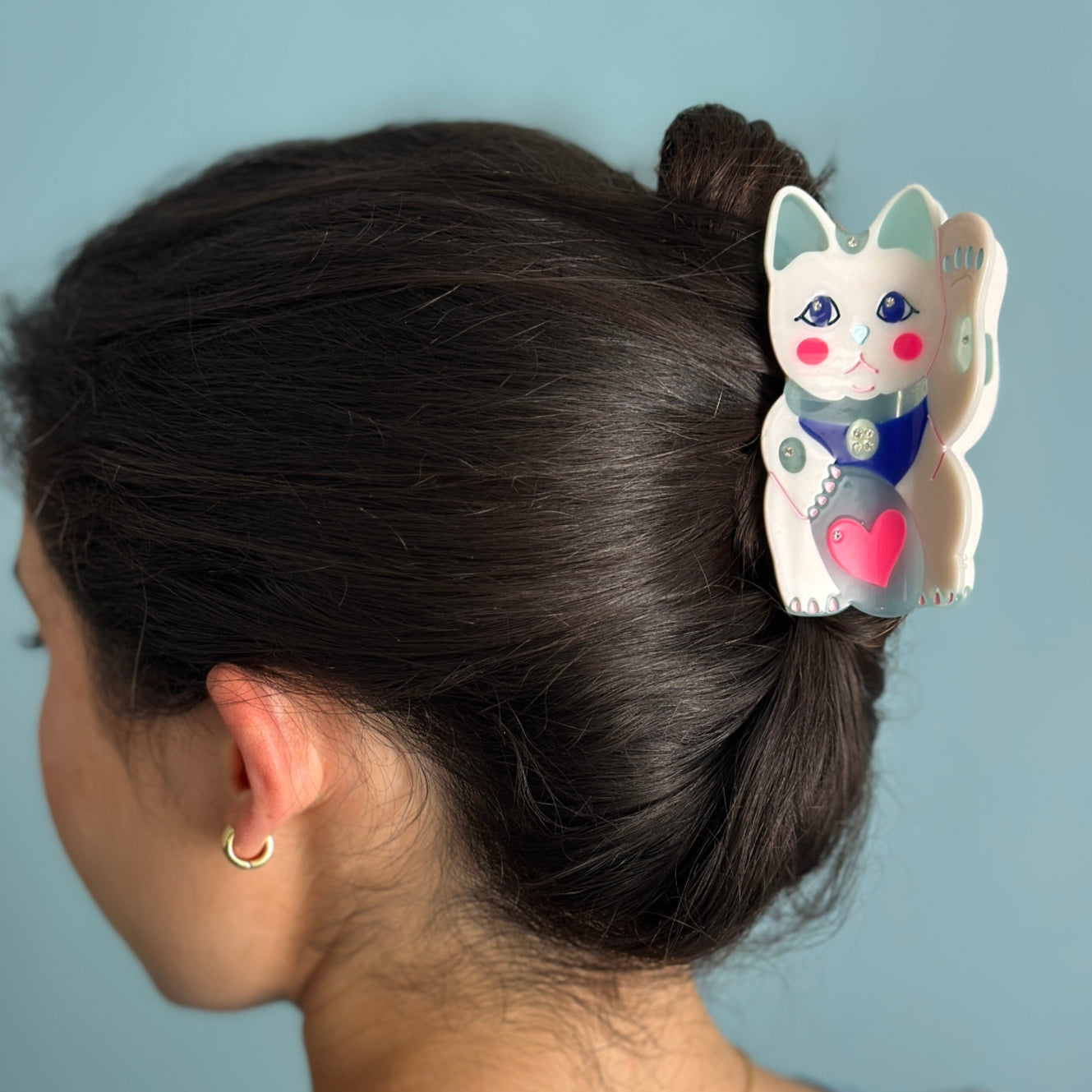Lucky cat hair claw clipped to dark hair; white cat with blue eyes and pink heart