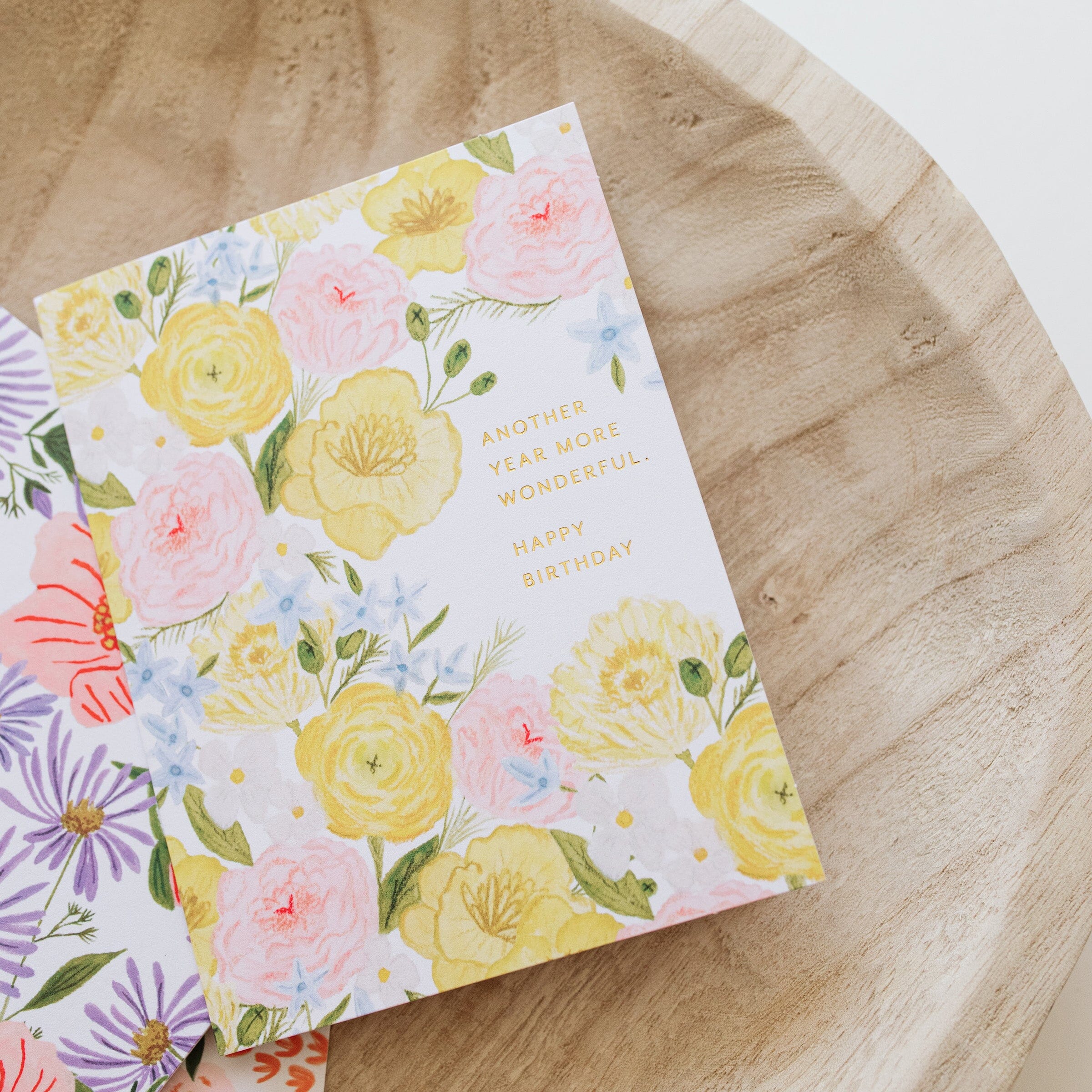 Birthday card angled; pastel florals with 'Happy Birthday' and 'Another year more wonderful'.