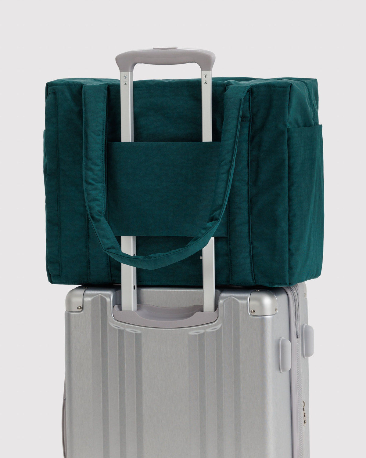 Teal carry-on tote bag attached to a rolling suitcase with a handle pass-through