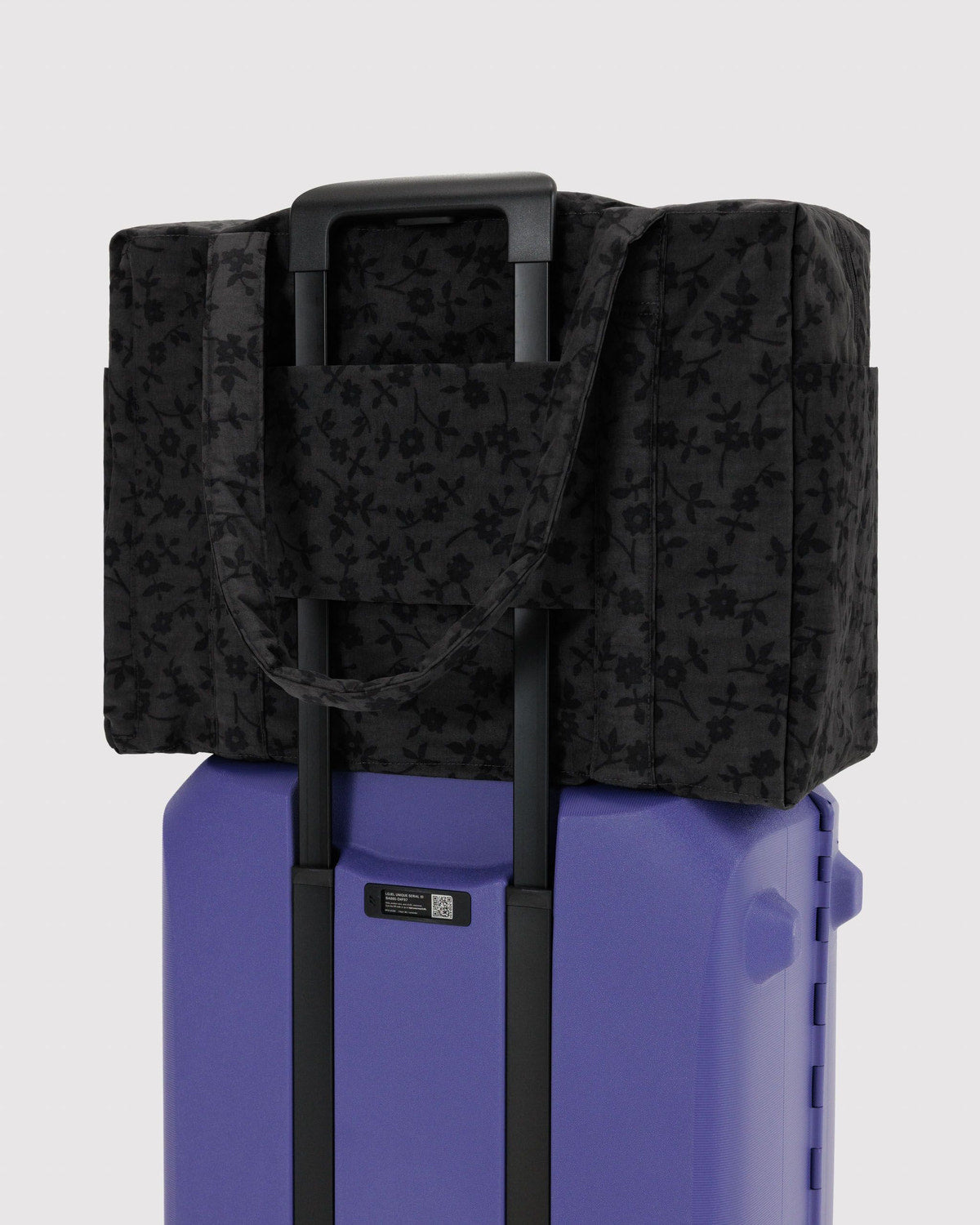 Charcoal floral carry-on tote bag over rolling suitcase with padded grab handles