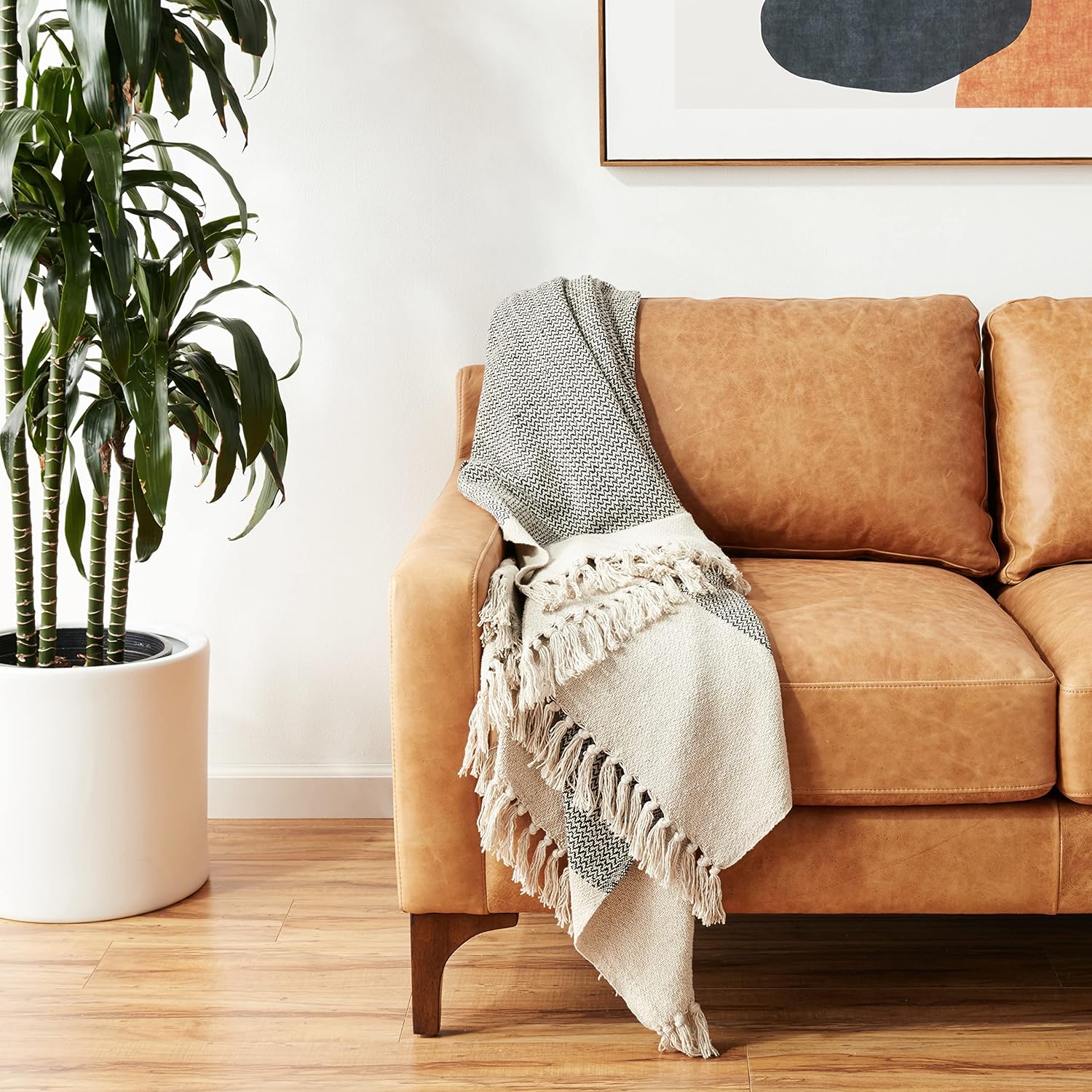 Grey knit throw blanket with long fringe, draped on a sofa