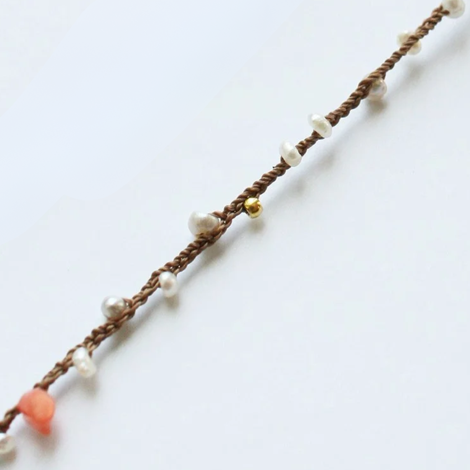 Braided bracelet detail with white pearls, gold beads, and orange charm