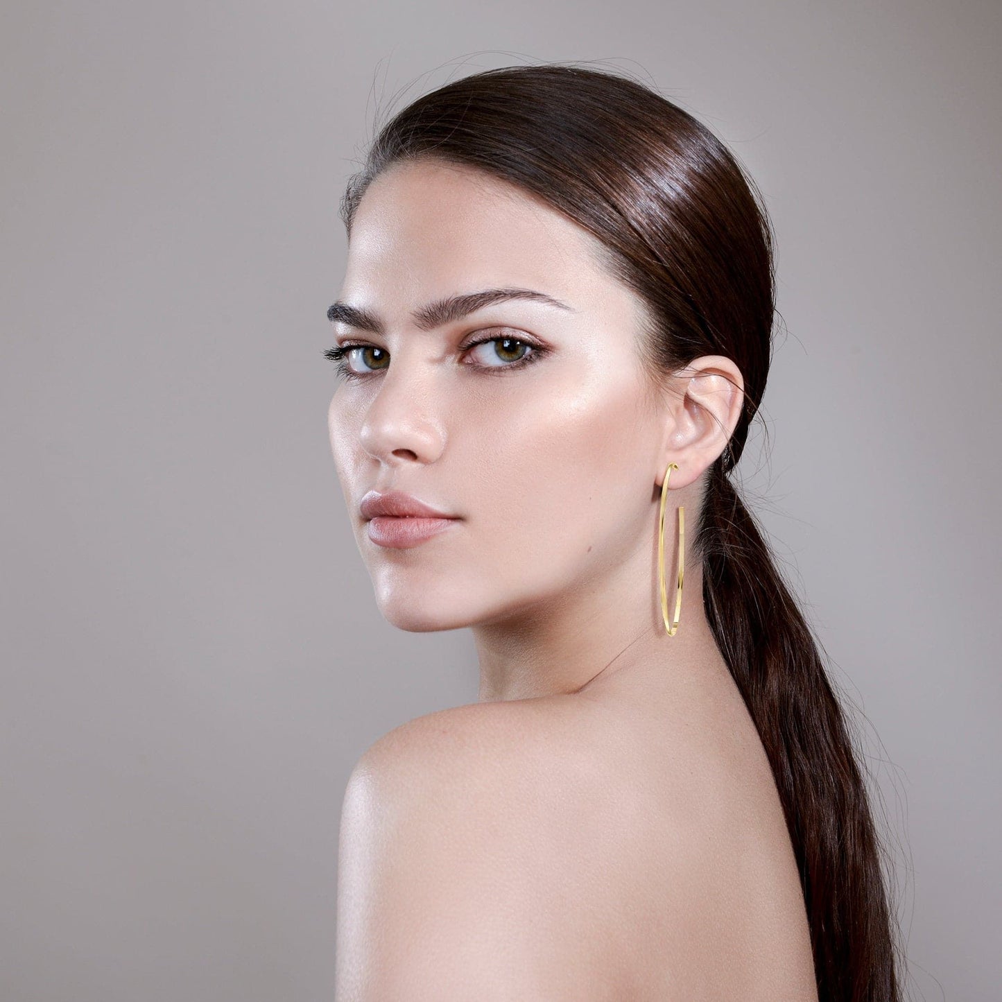 Gold hoop earrings worn on ear, slim oval hoop with clasp