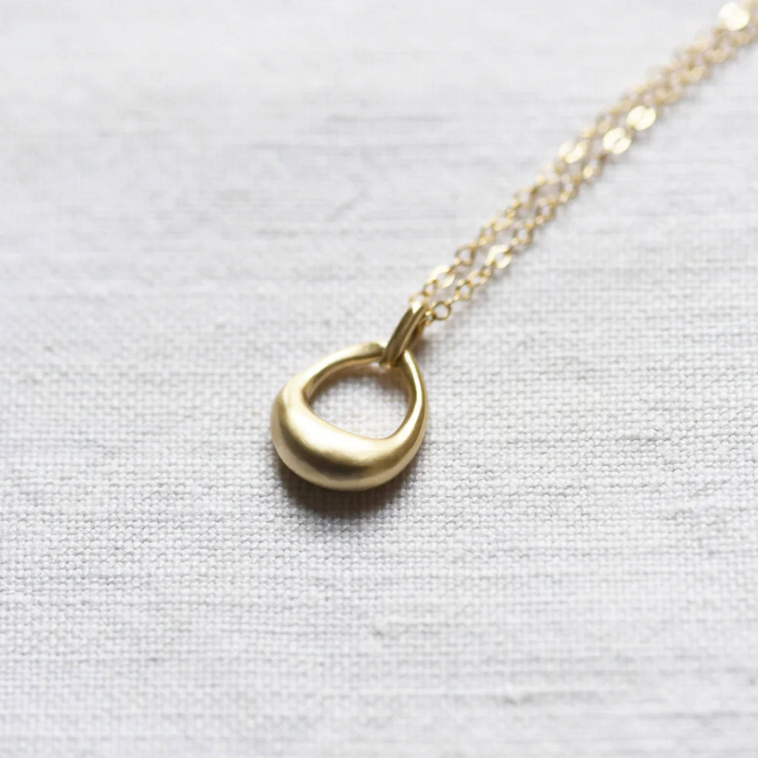 Gold open-circle pendant necklace with thin link chain, close-up