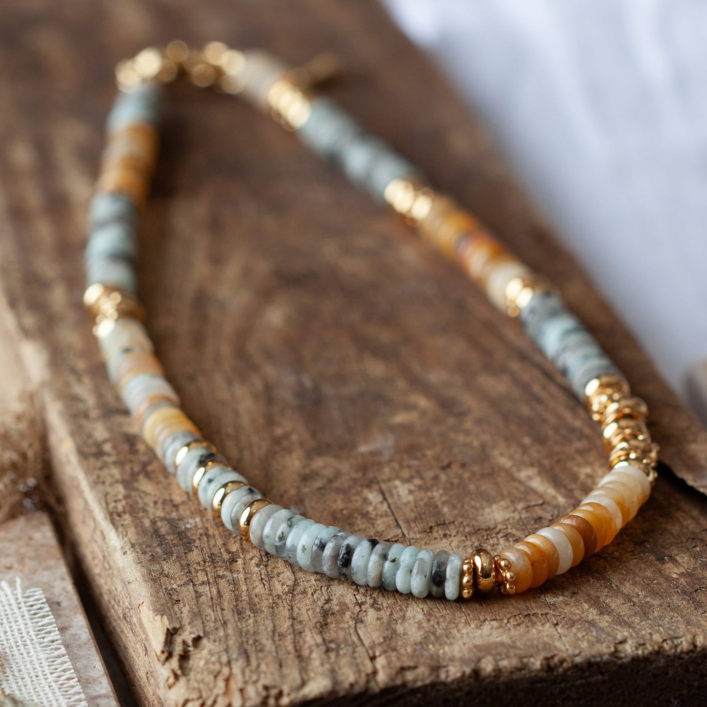 Close-up of beaded gold-tone necklace: light blue/gray heishi with gold spacer beads
