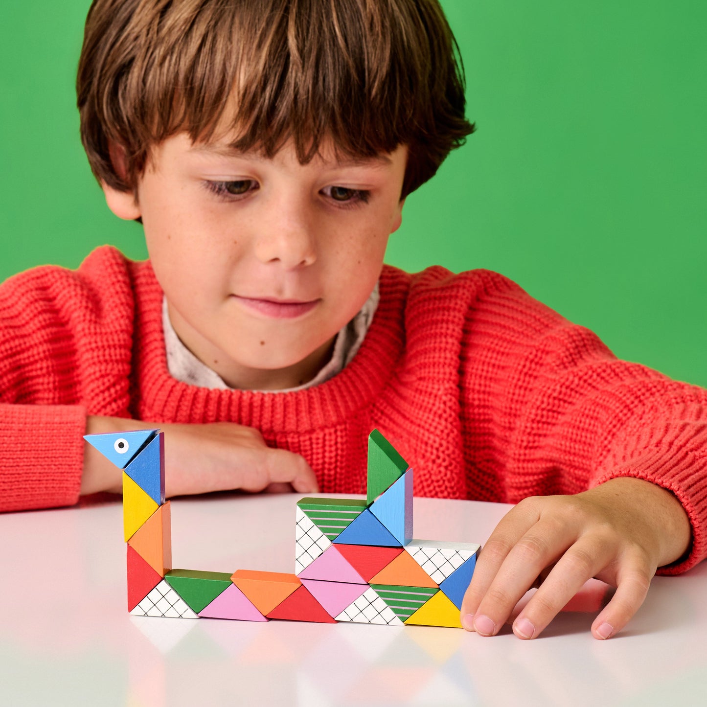 Colorful geometric puzzle tiles with white grid faces, held and assembled by a child