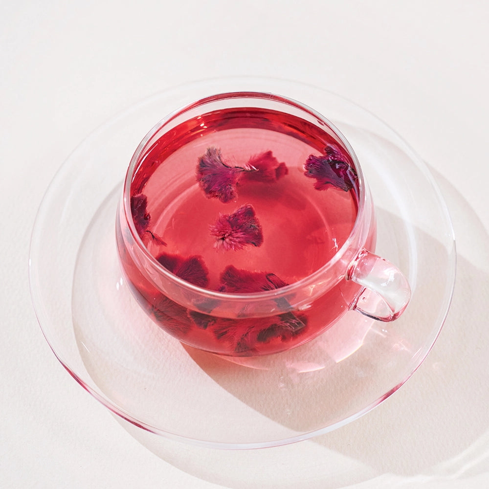 Clear glass mug of pink flower tea with visible dried blossoms, isolated view