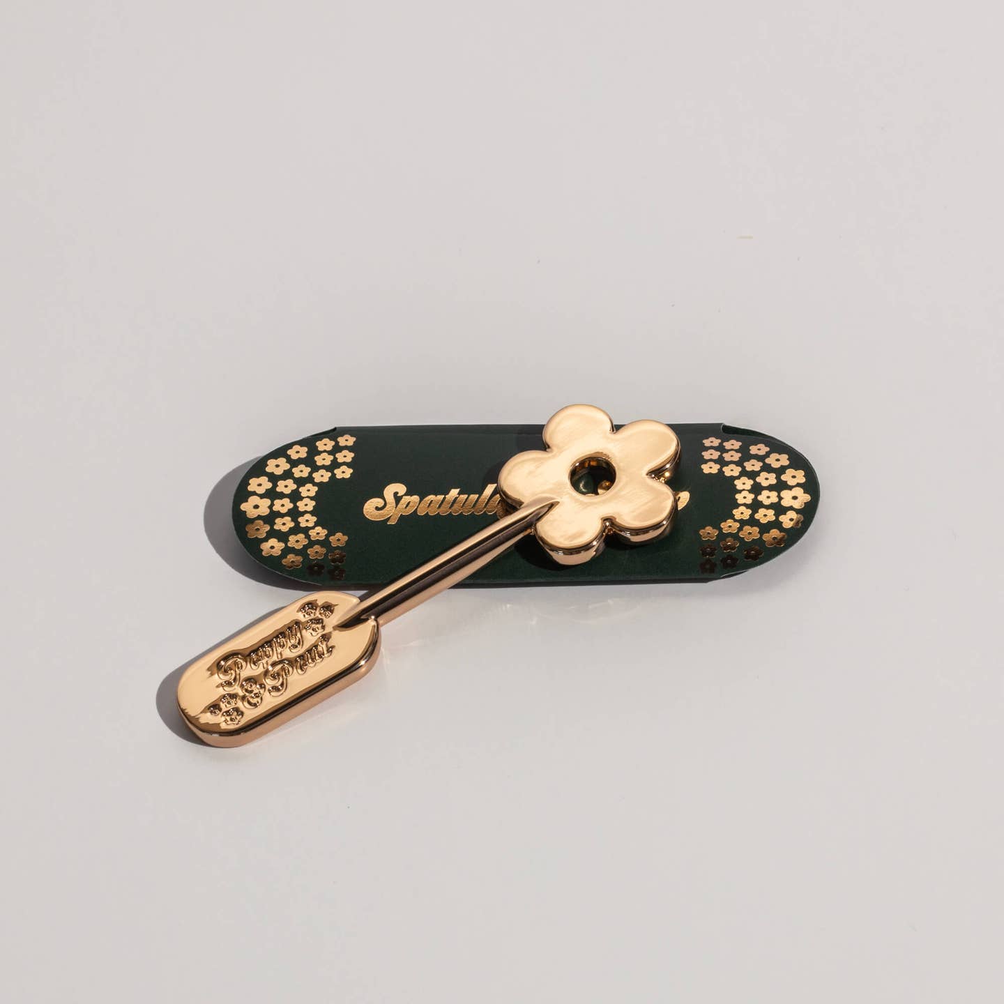 Gold lip care spatula with daisy-shaped handle and engraved floral pattern on the scoop
