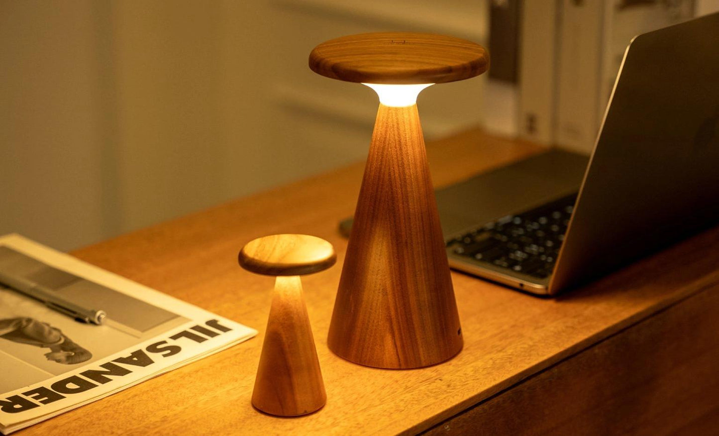 Sylva mini ash table lamp, foreground, lit with wooden base and cream conical shade