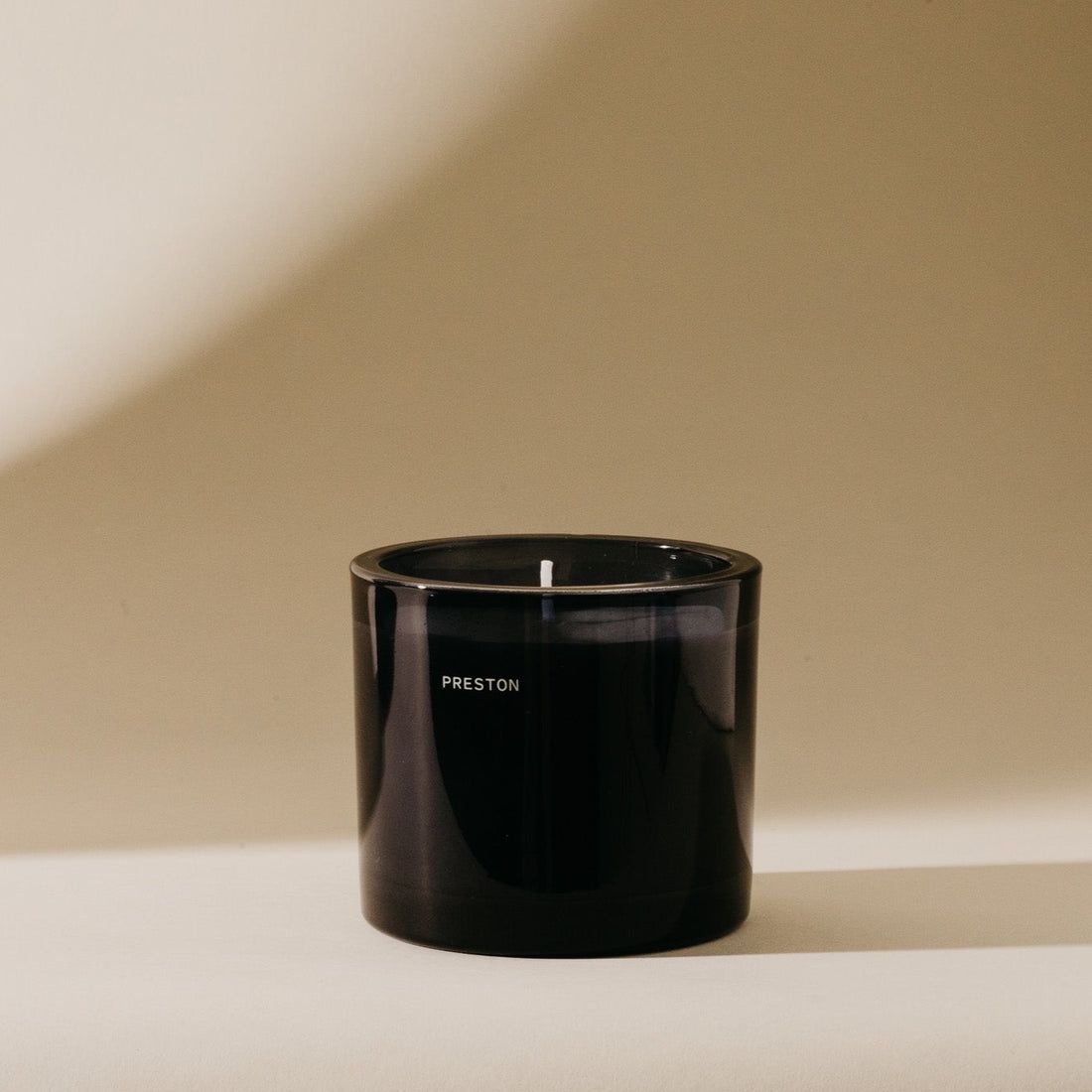 Black glass jar candle with lit wick and minimal label on the front