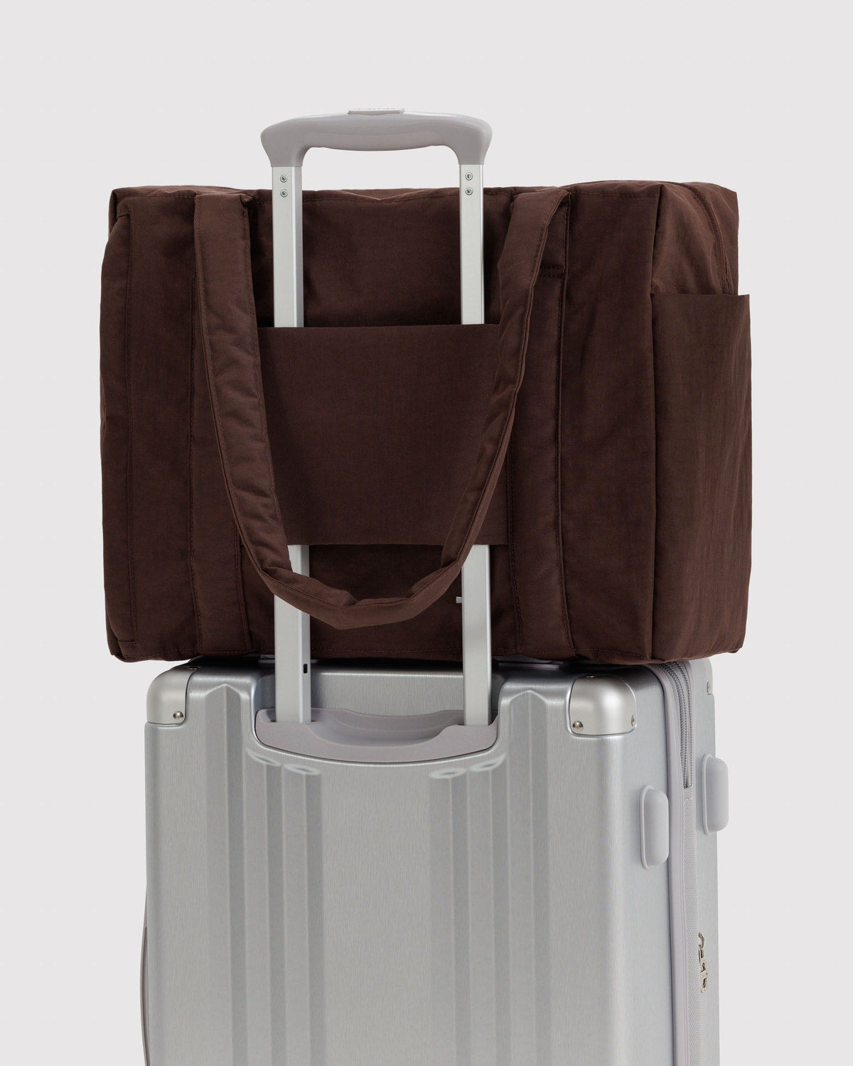 Brown carry-on tote bag attached to a rolling suitcase with a handle pass-through