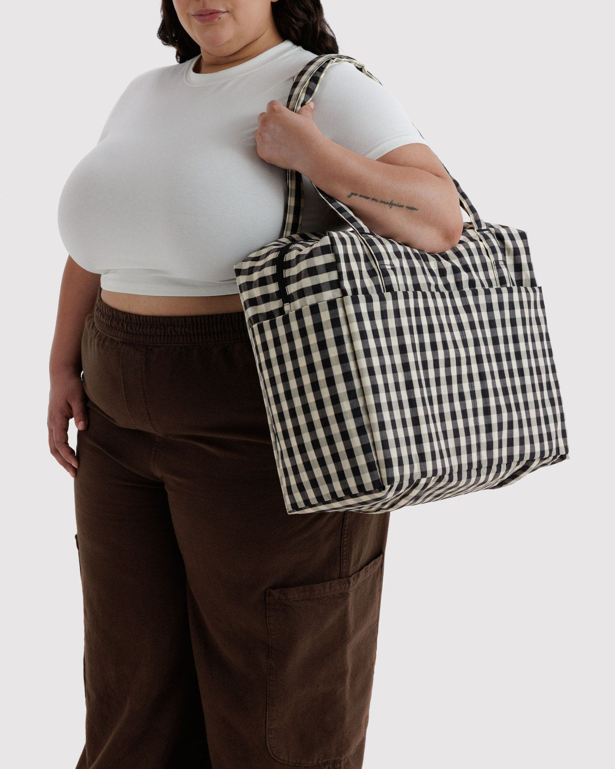 Carry-on bag in black-and-white gingham carried by model, with side pocket