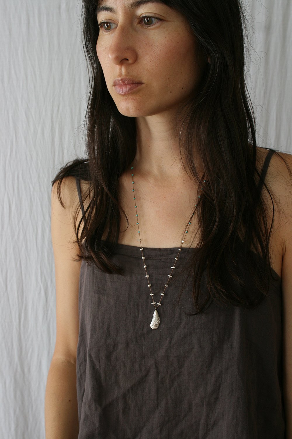Beaded shell pendant necklace worn by model, turquoise beads and white beads