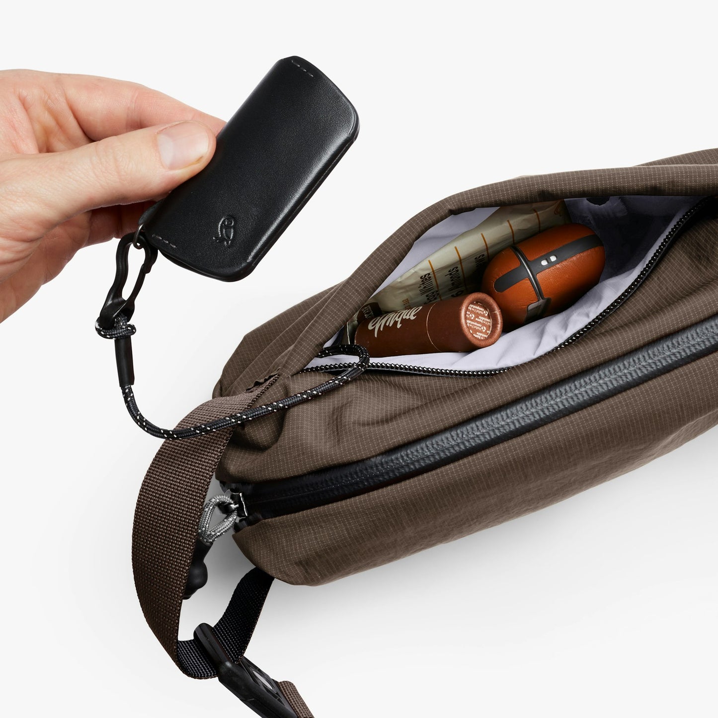 Mini sling bag with zip top opened; items and hand holding a small black pouch.