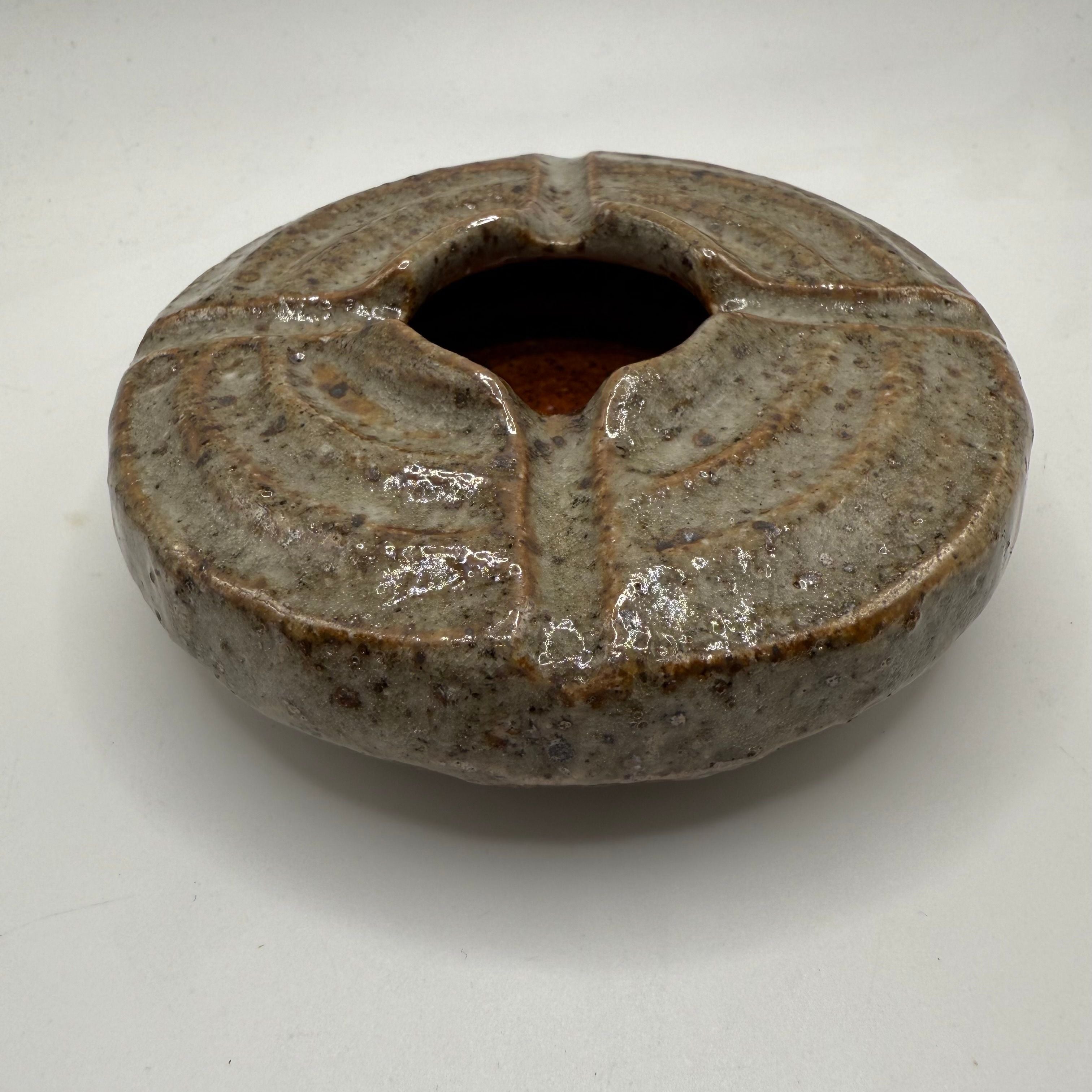 Ceramic ashtray, round bowl with raised rim and circular center opening.