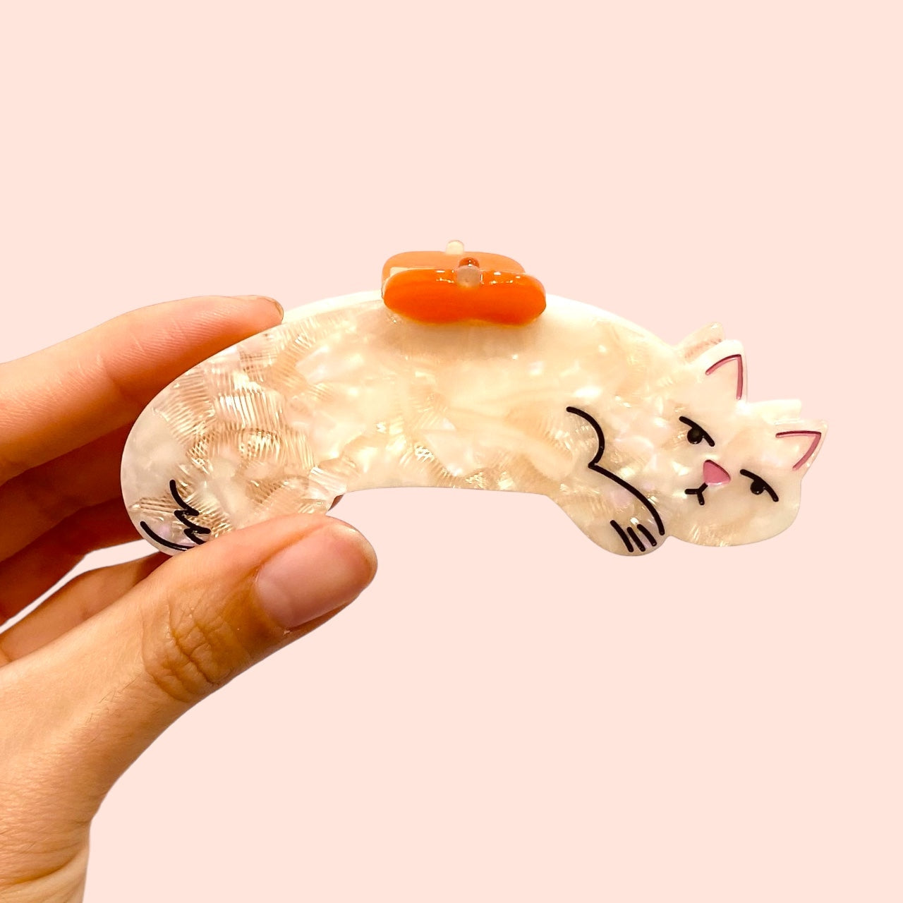 Cream cat hair claw held in hand, orange clip on top and kitty face design