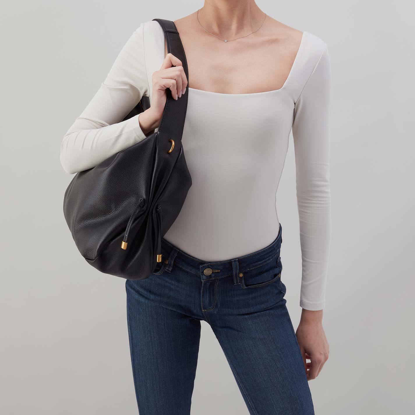 Black hobo bag carried on shoulder with side ties and gold-tone hardware