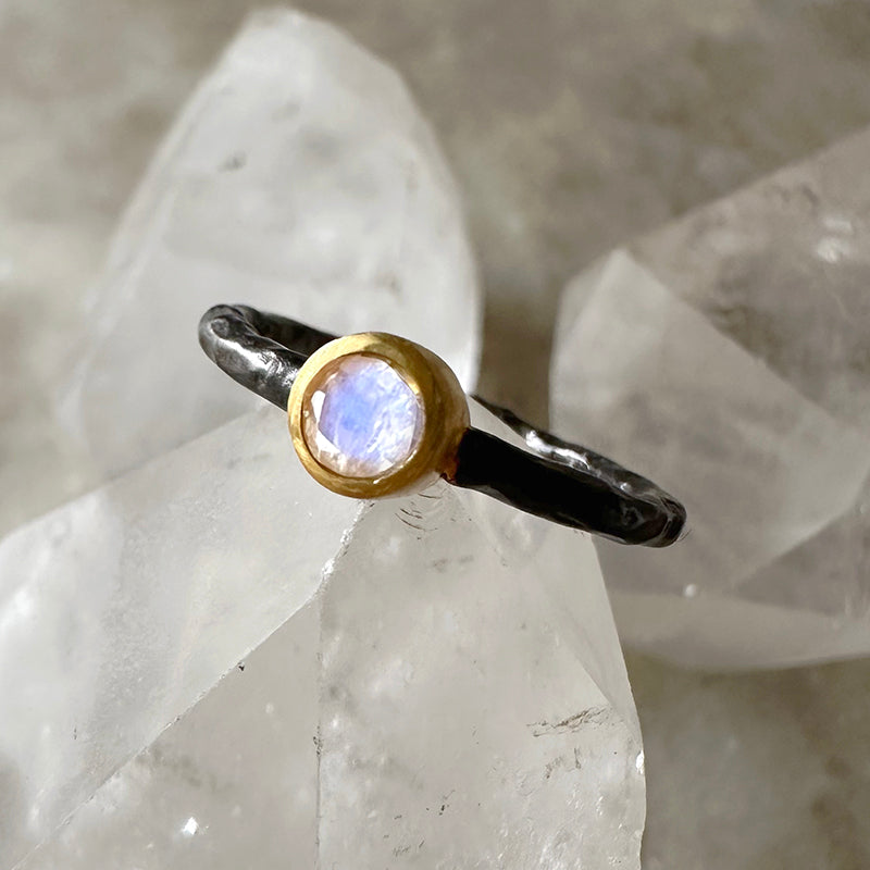 Moonstone ring with oval rainbow-blue stone, oxidized silver band, and gold bezel