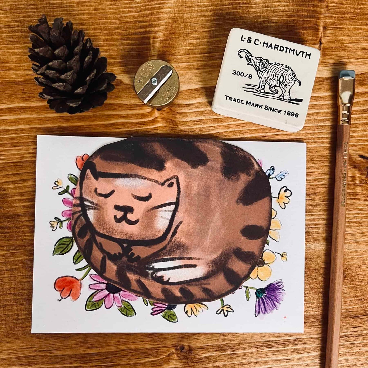 Curled-up cat greeting card with cartoon brown cat and floral accents