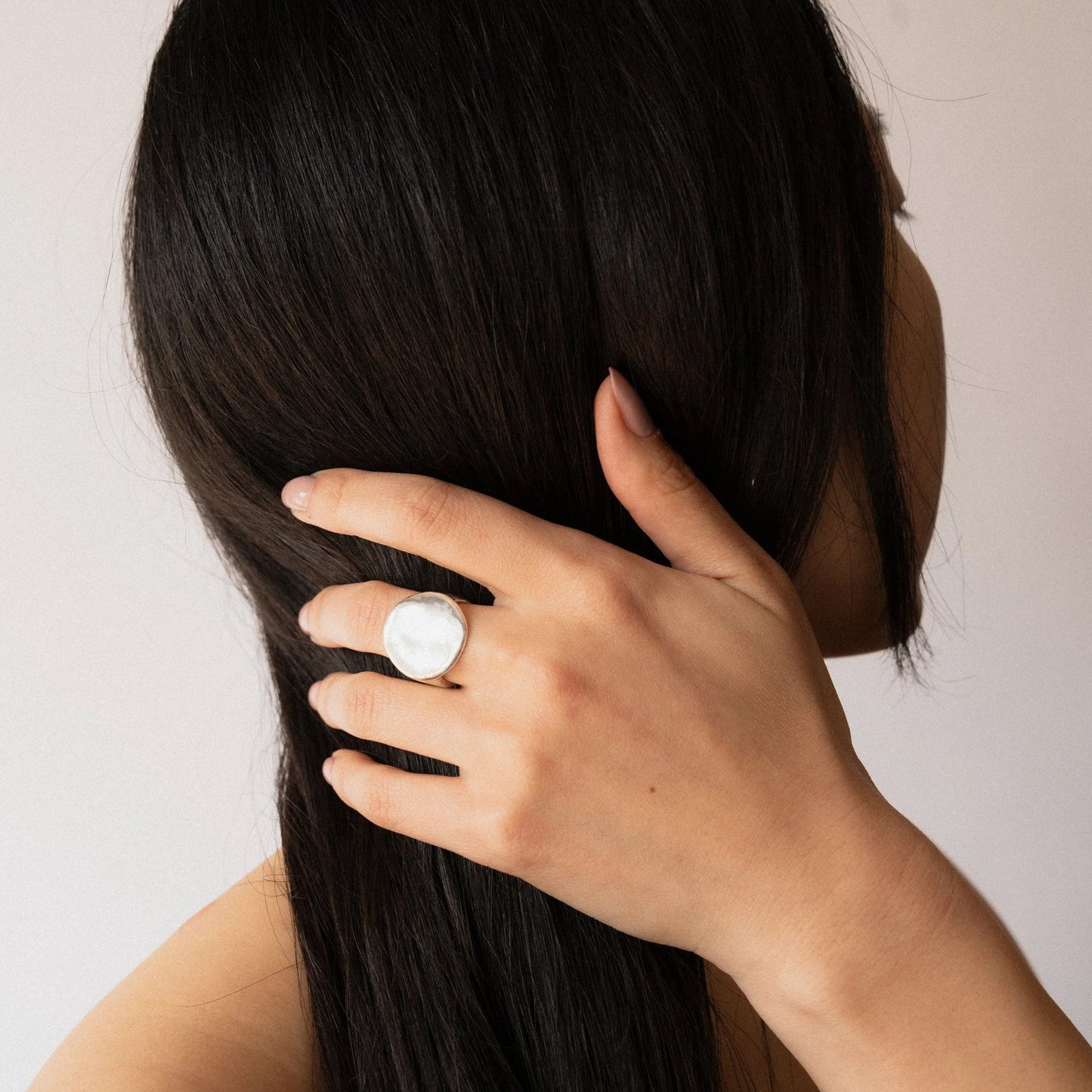 Silver coin-shaped statement ring with hammered texture, worn on finger