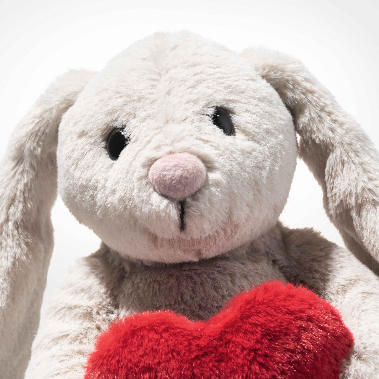 Close-up of light gray plush rabbit with pink nose and red heart