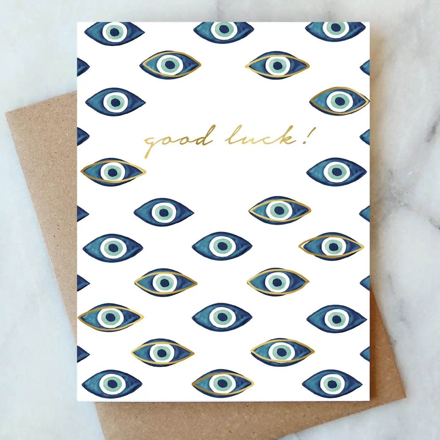 Good luck greeting card with blue evil eye pattern and gold script, on kraft envelope