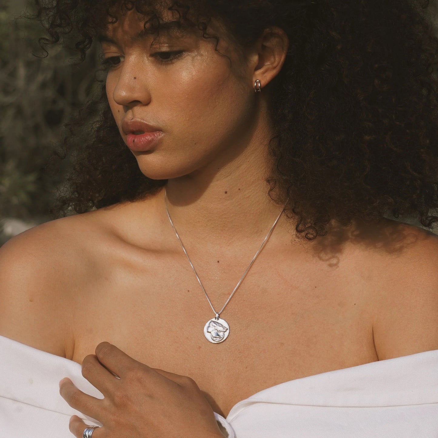 Silver pendant necklace with circular medallion on thin chain, worn at collarbone