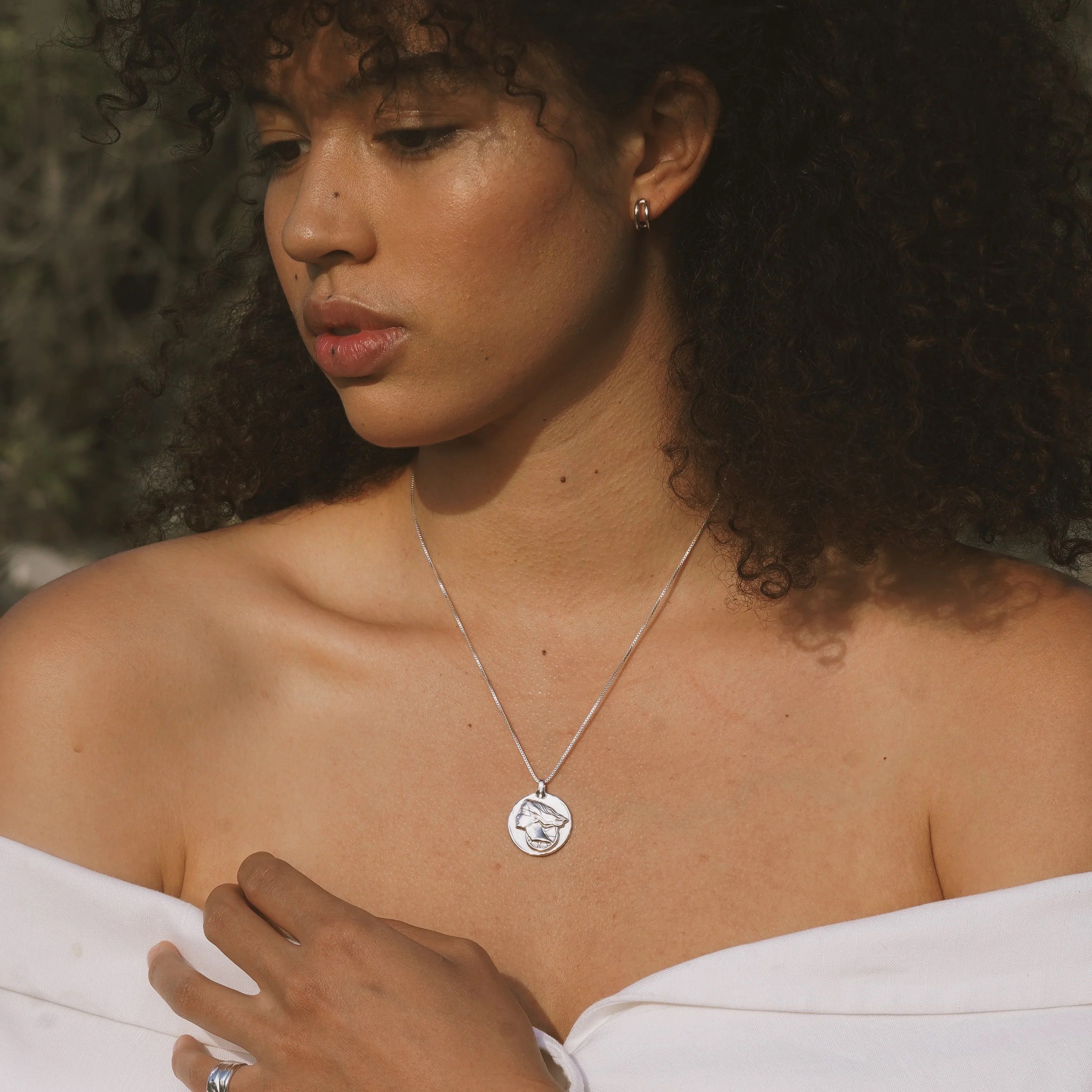 Silver pendant necklace with circular medallion on thin chain, worn at collarbone