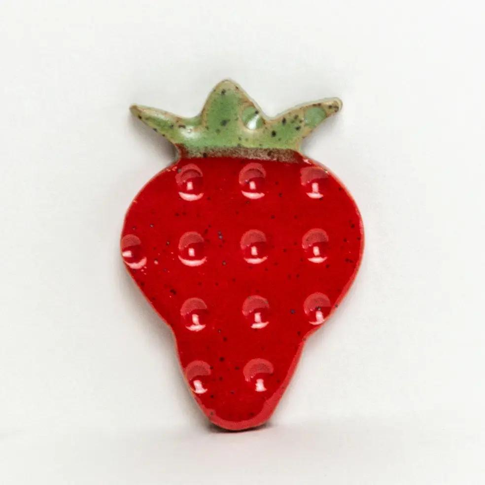 Strawberry-shaped red ceramic refrigerator magnet with green leafy top and speckled glaze