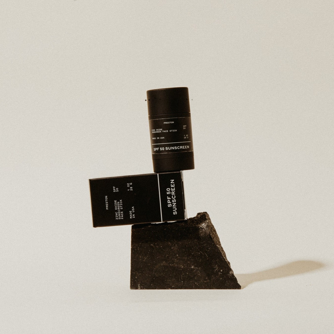 Black sunscreen stick and SPF 50 sunscreen box with product texture pieces