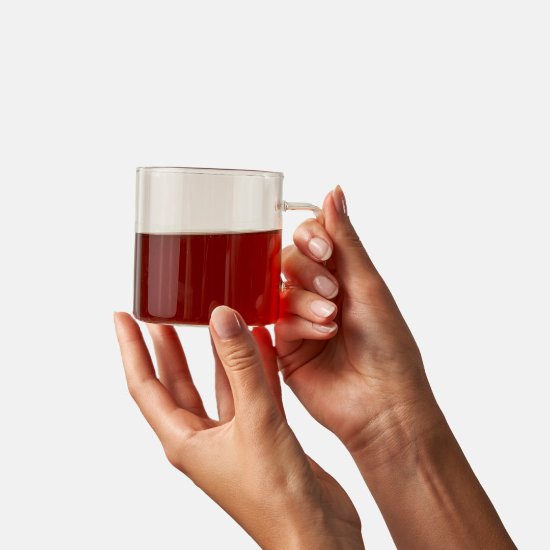 Organic black tea in clear glass cup, hands holding warm brown tea