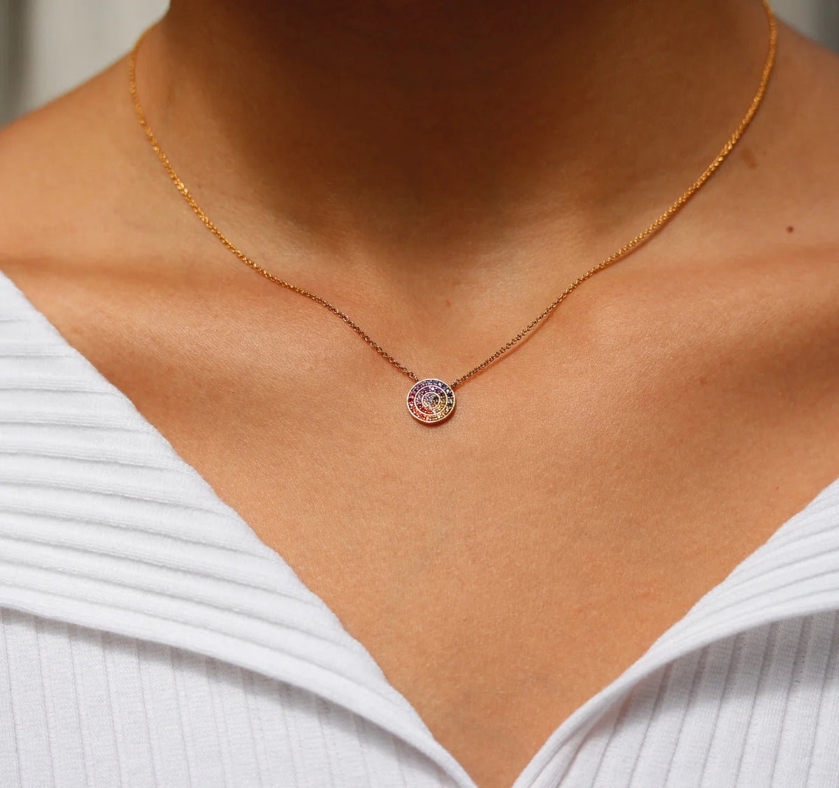 Small round rainbow pendant necklace on a gold chain, worn at the neckline